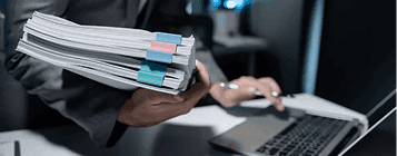 Person holding documents near laptop