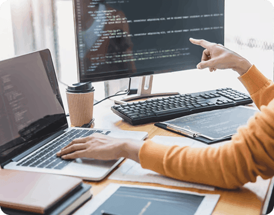 Developer pointing at dual monitors displaying code in an office