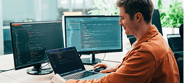 Developer coding on laptop with dual monitors