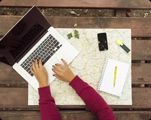 Person working on a laptop over a map on a wooden table