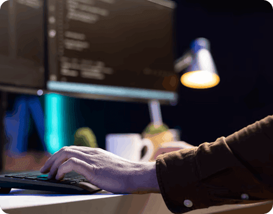 Person typing on a keyboard with computer screen and lamp in background