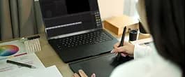 Designer sketching on a tablet beside a laptop