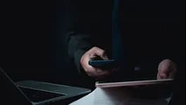 Person holding a phone above a laptop in low light