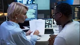 Security engineers reviewing a report beside monitors